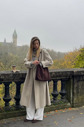 a lady in a grey top, a brown long wool coat and a pair of white pants